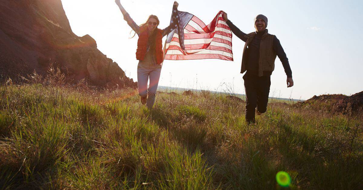 Couple holding American flag running through a field